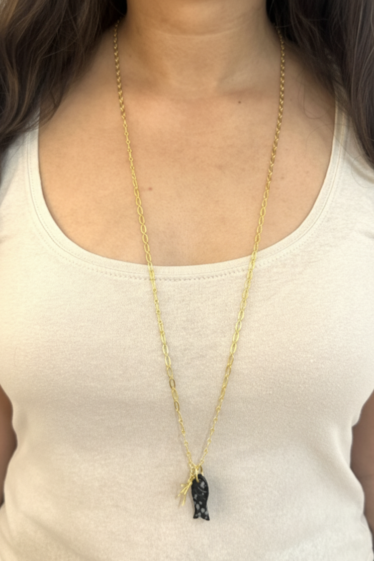 Gold necklace with a pendant on a person wearing a white tank top