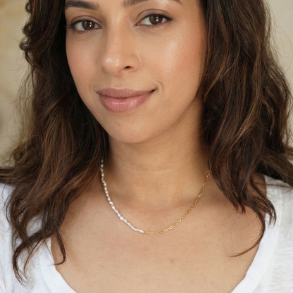 Woman with wavy hair wearing a white shirt and pearl necklace against a neutral background