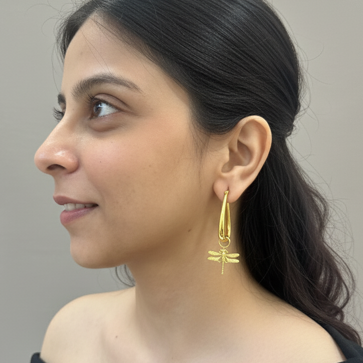 Woman wearing gold dragonfly emberly hoops earrings against a neutral background