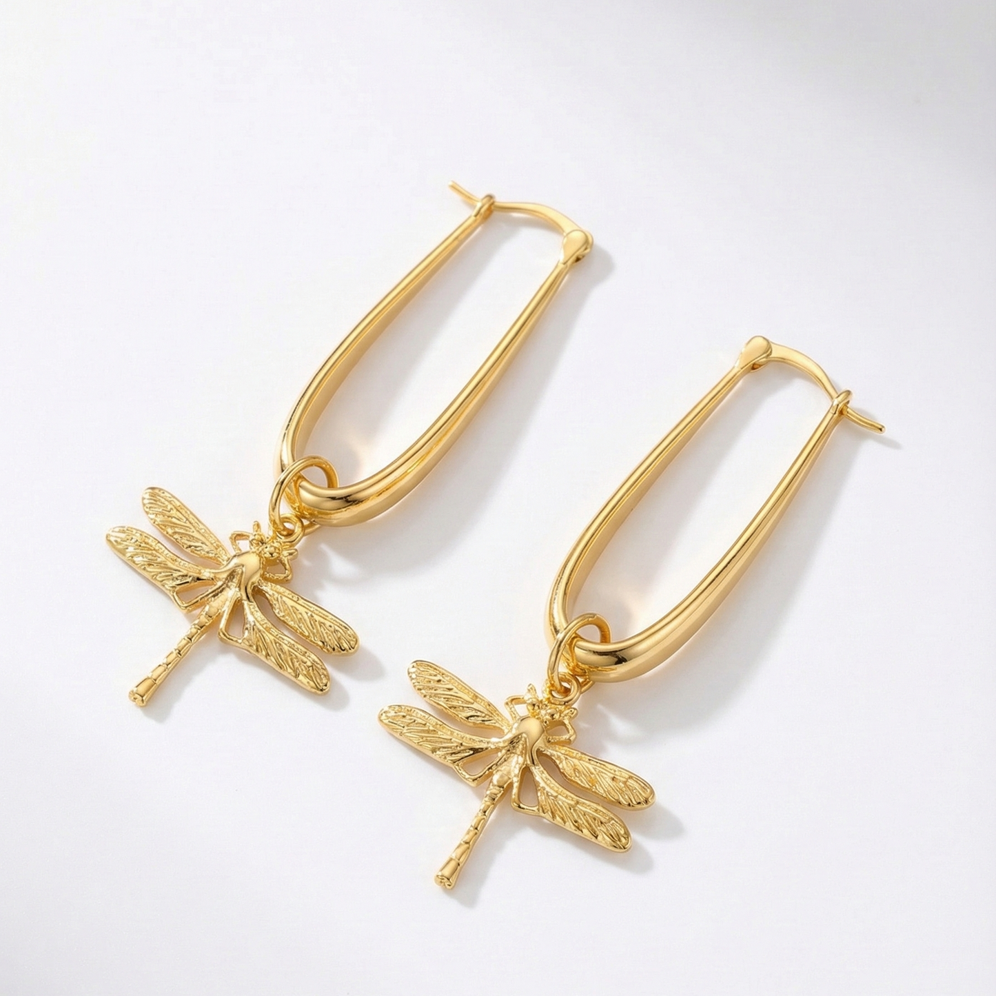 Gold hoop earrings with dragonfly charms on a light gray background