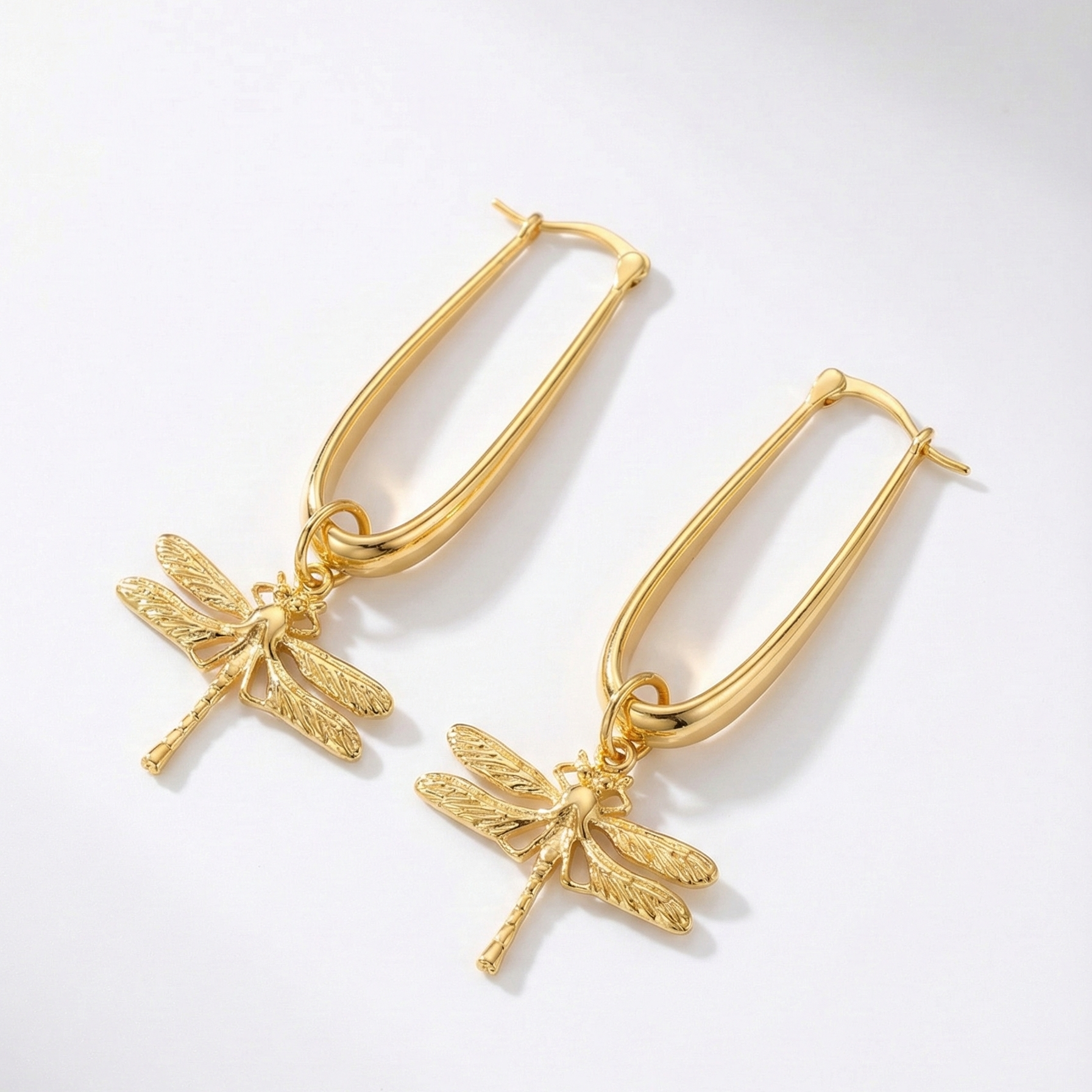 Gold hoop earrings with dragonfly charms on a light gray background