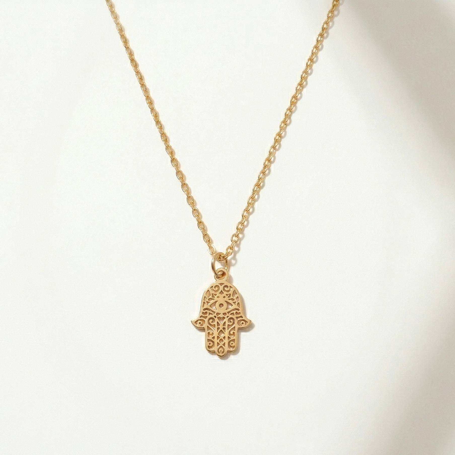 Gold necklace with a hamsa hand pendant on a white background