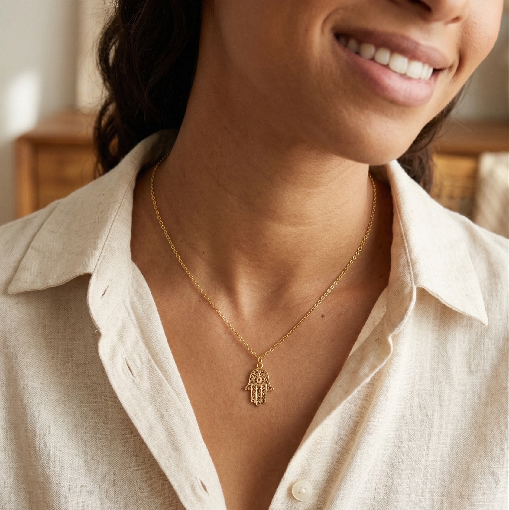 Woman wearing a gold necklace with a hamsa hand pendant, smiling.