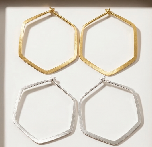 Two pairs of hexagonal hoop earrings, one gold and one silver, on a white background.