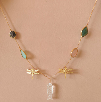 Necklace with gold chain, green and blue stone pendants, and insect-shaped charms on a beige background