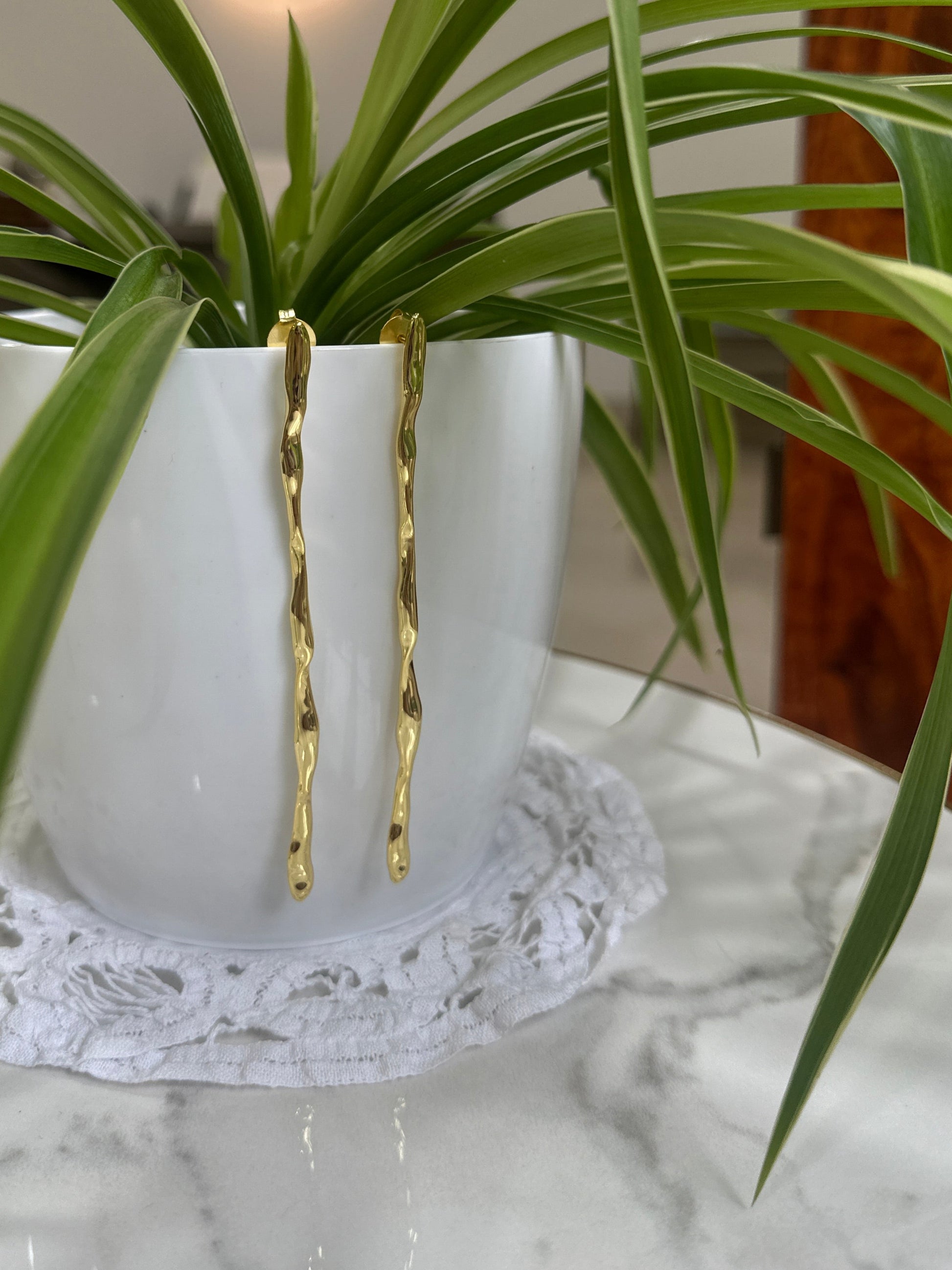 Gold hairpin on a white vase with green plant leaves