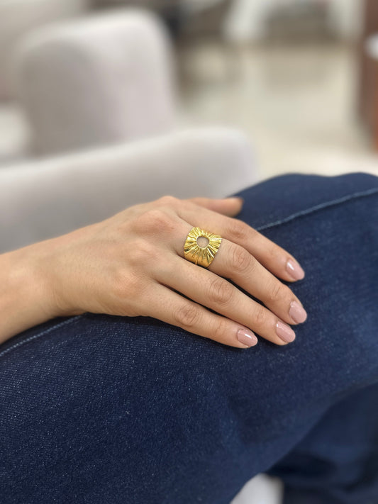 Hand wearing a gold ring with a sun design 
