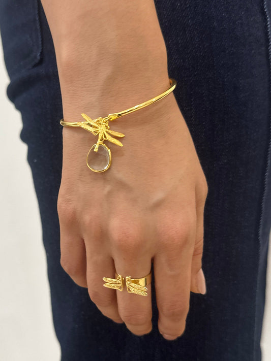 Hand wearing gold bracelet and ring on a white surface