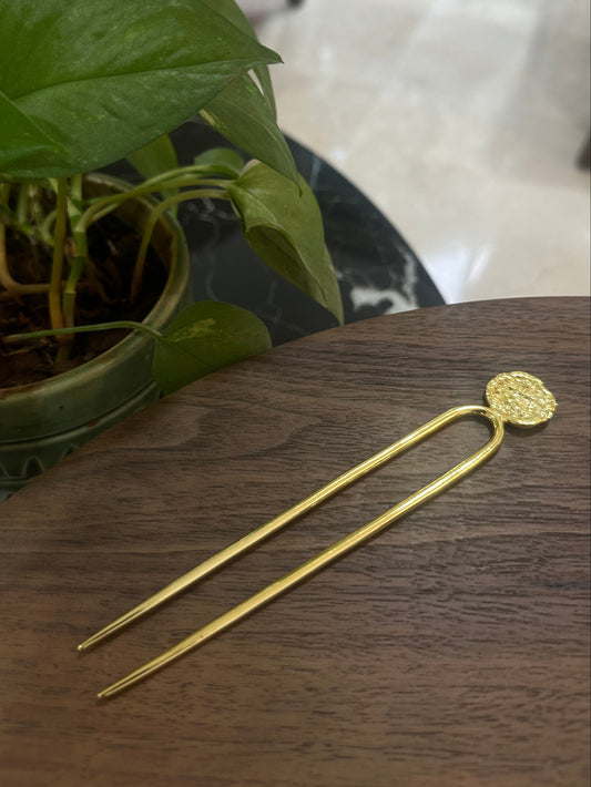 Gold hairpin on a wooden surface with a plant in the foreground