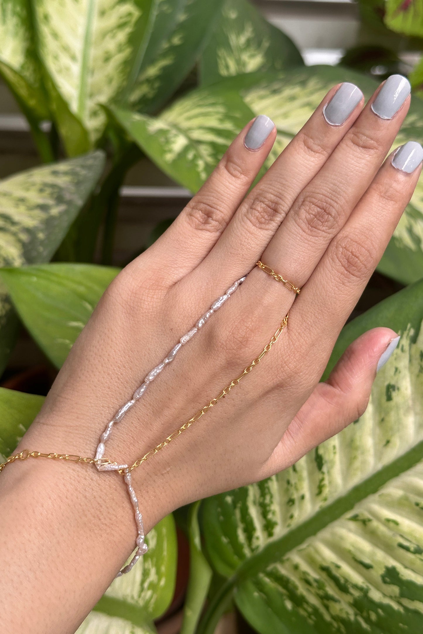 Hand with gold and silver chain bracelets against a green leafy background