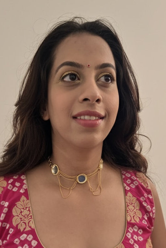 Woman wearing a pink and gold patterned top with gold jewelry against a plain background