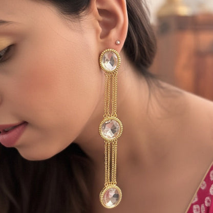 Woman wearing gold earrings with clear gemstones, blurred background
