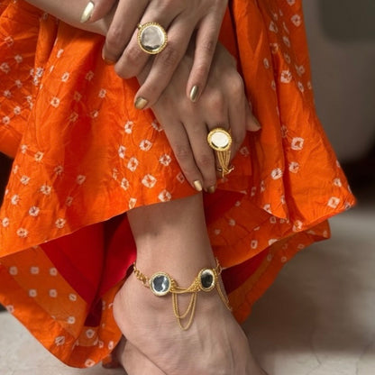 Close-up of a person's feet wearing gold anklets and rings, with an orange garment.