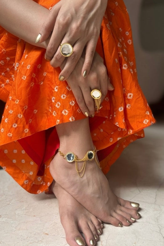 Close-up of a person's feet wearing gold anklets and rings, with an orange garment.