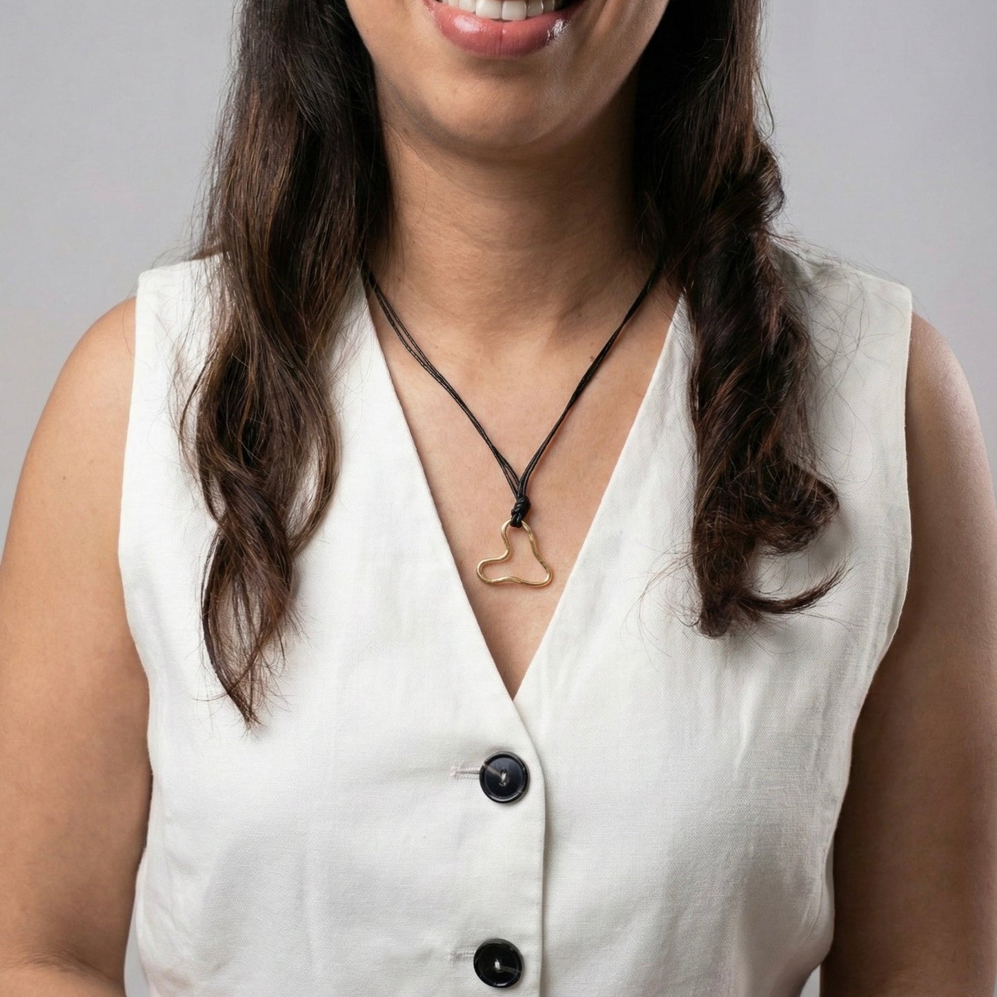 Woman wearing a white sleeveless top with black buttons and a necklace against a gray background