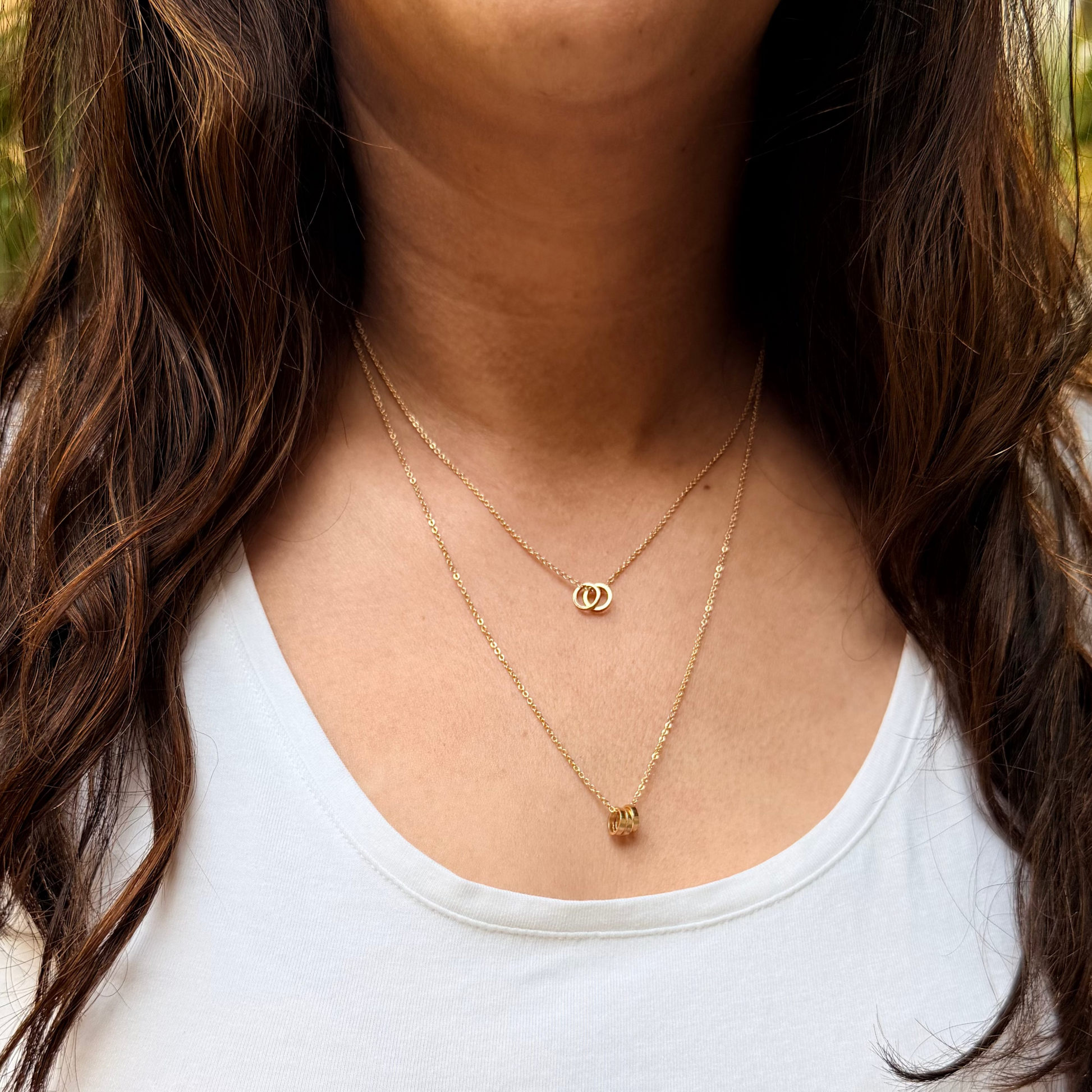 Woman wearing a white tank top with gold necklaces, sitting outdoors.
