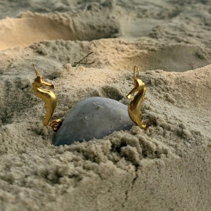 Gold seahorse earrings on a sandy background with shells and pearls.