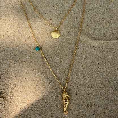 Gold necklace with a seahorse and shell pendant .