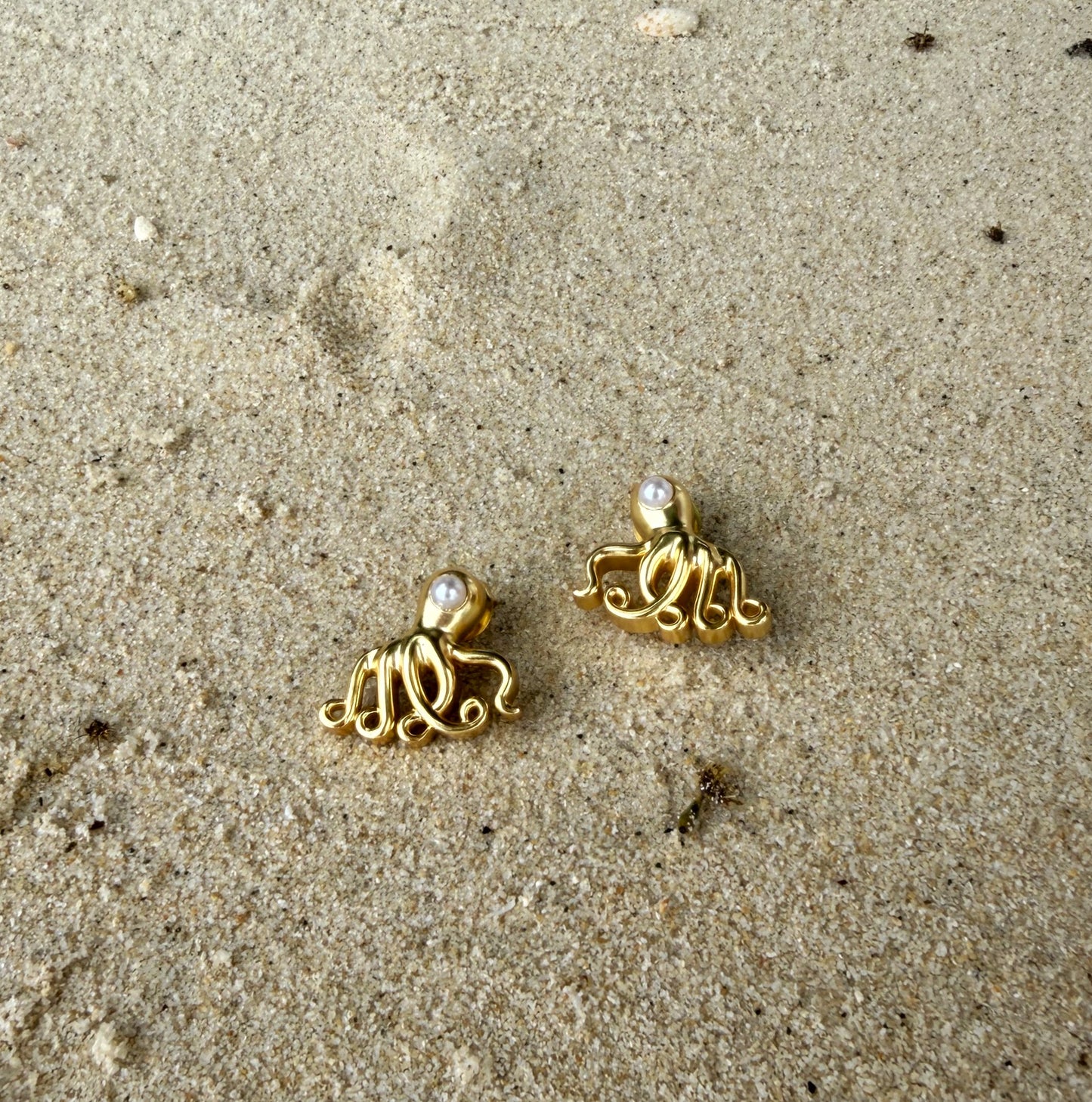 Gold octopus earrings on a sandy surface