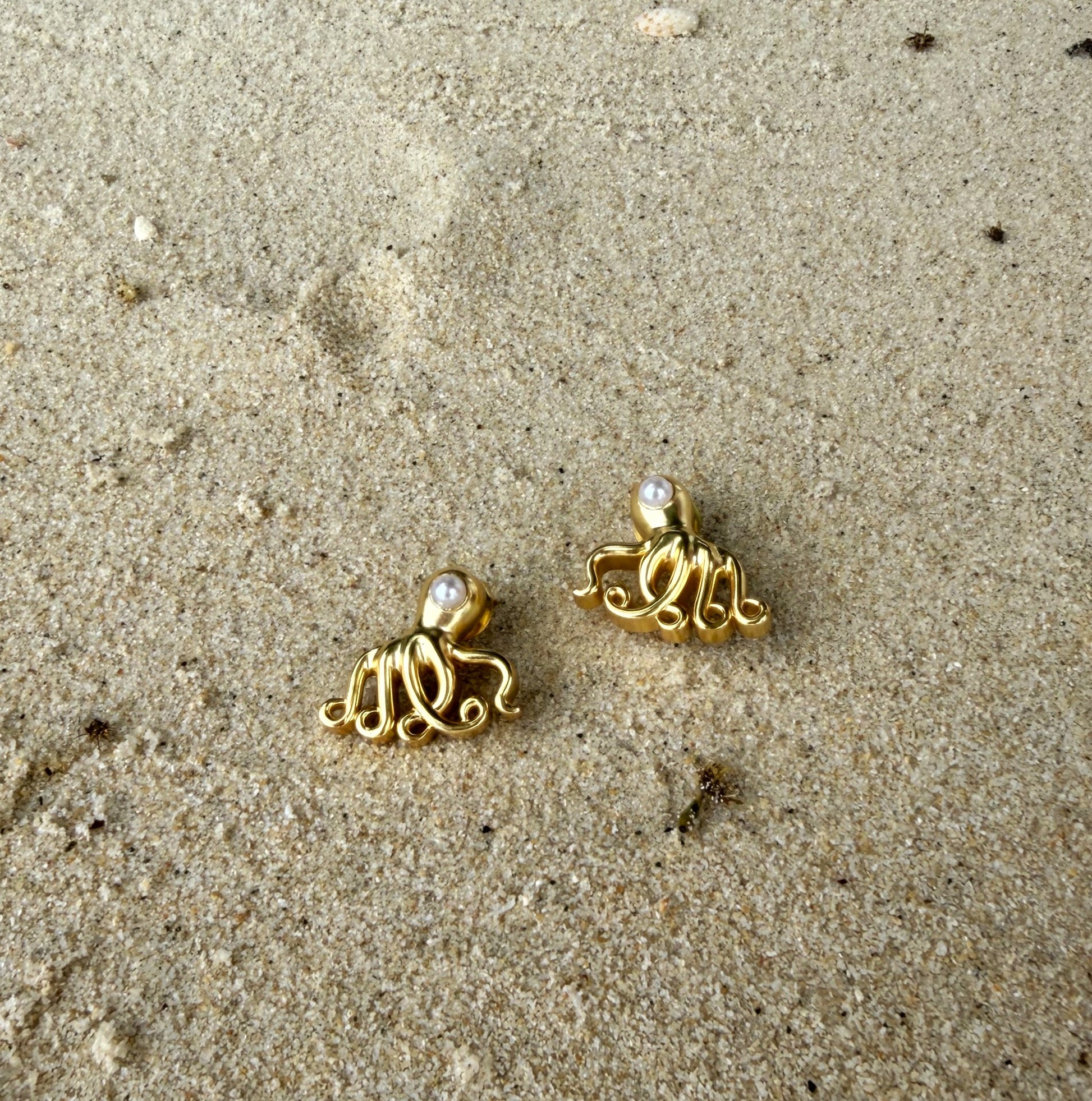 Gold octopus earrings on a sandy surface
