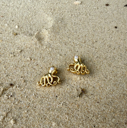 Gold octopus earrings on a sandy surface
