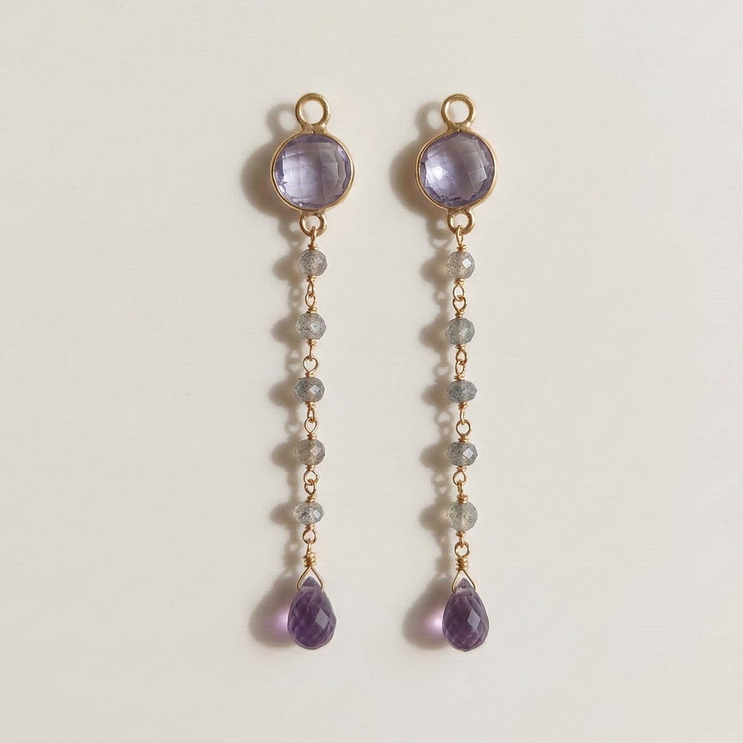 Pair of gold earrings with purple gemstones on a light gray background