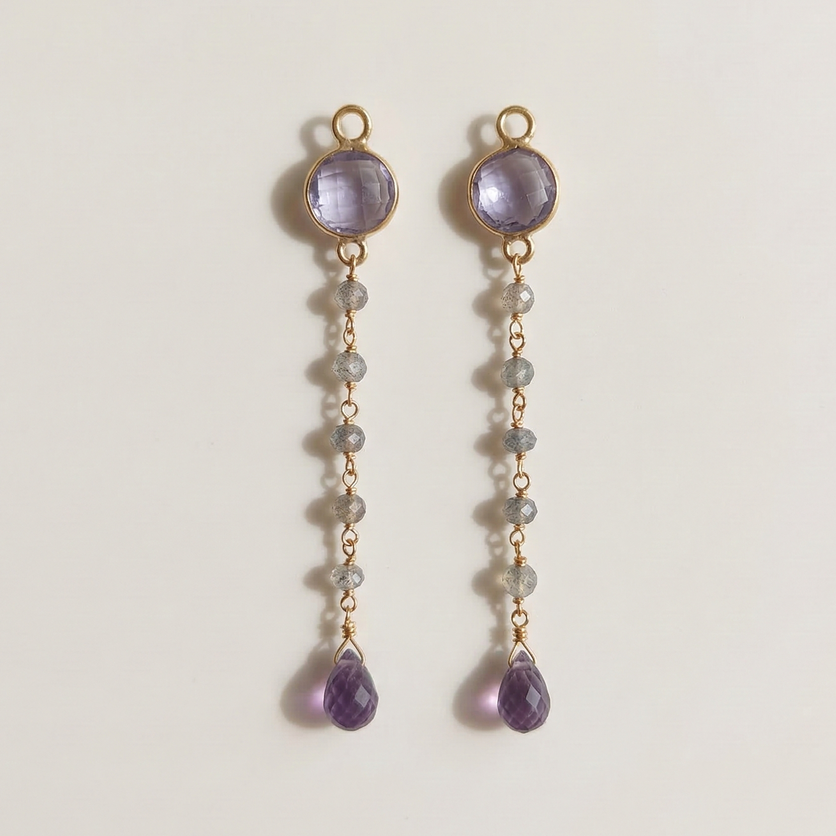 Pair of gold earrings with purple gemstones on a light gray background