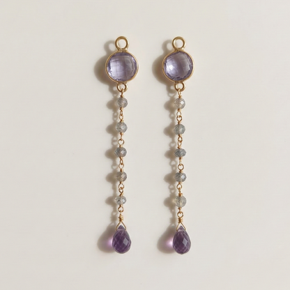 Pair of gold earrings with purple gemstones on a light gray background