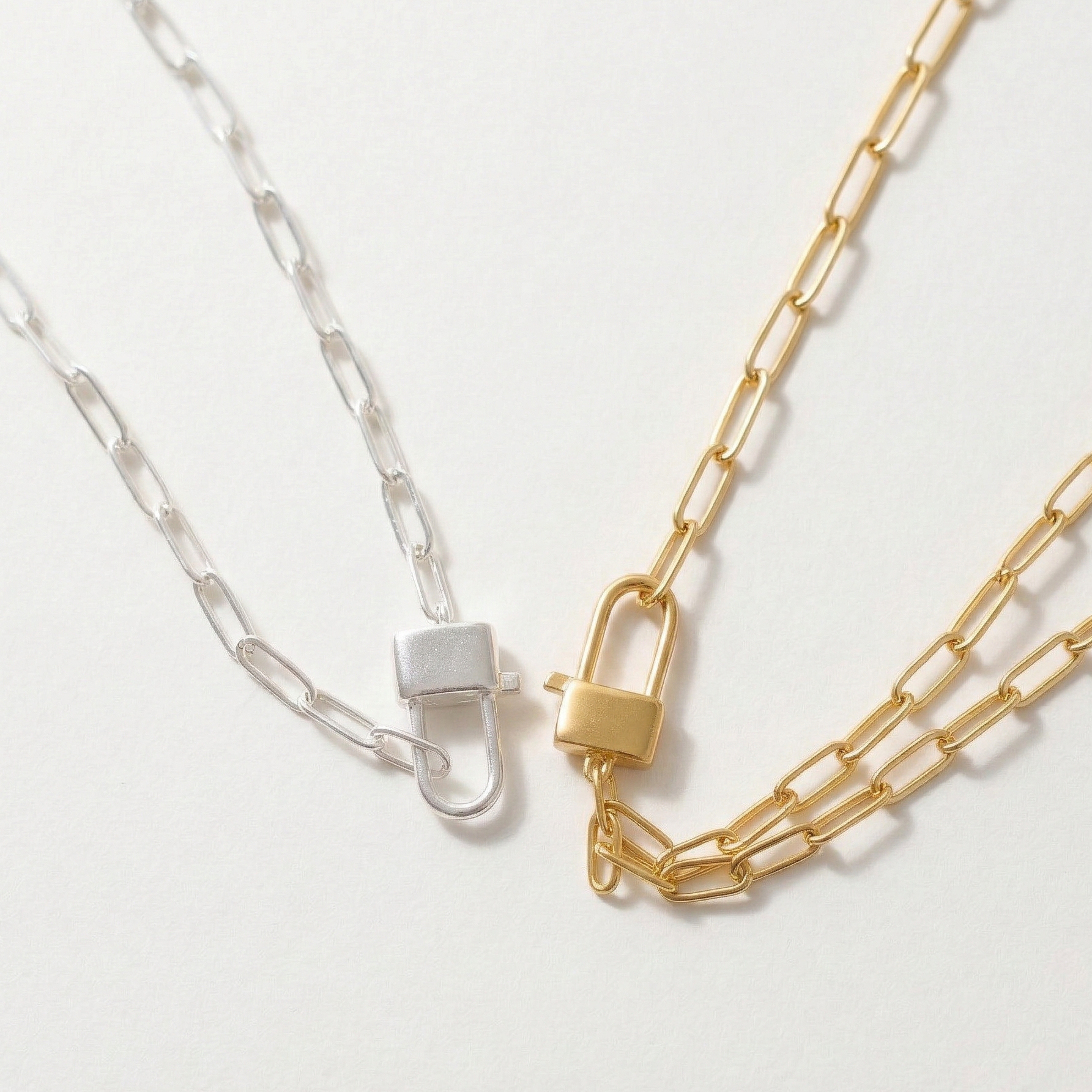 Two chain necklaces, one gold and one silver, on a light gray background.