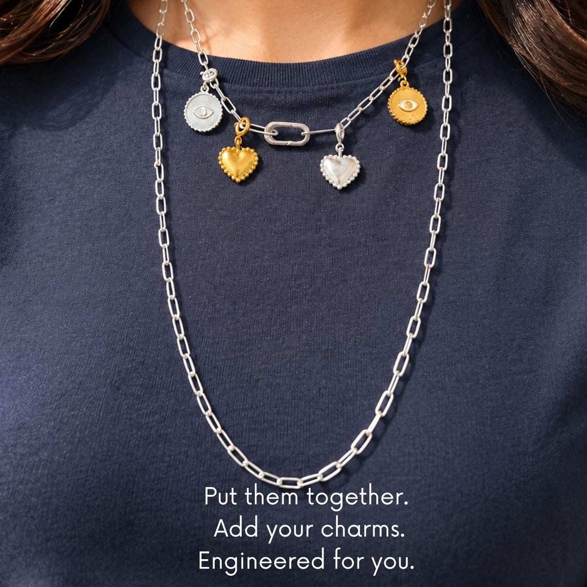 A close-up of a person wearing a layered necklace set over a navy blue shirt. The necklace features a silver chain with heart charms, a silver link chain, and gold-toned charms, with text at the bottom reading 'Put them together.