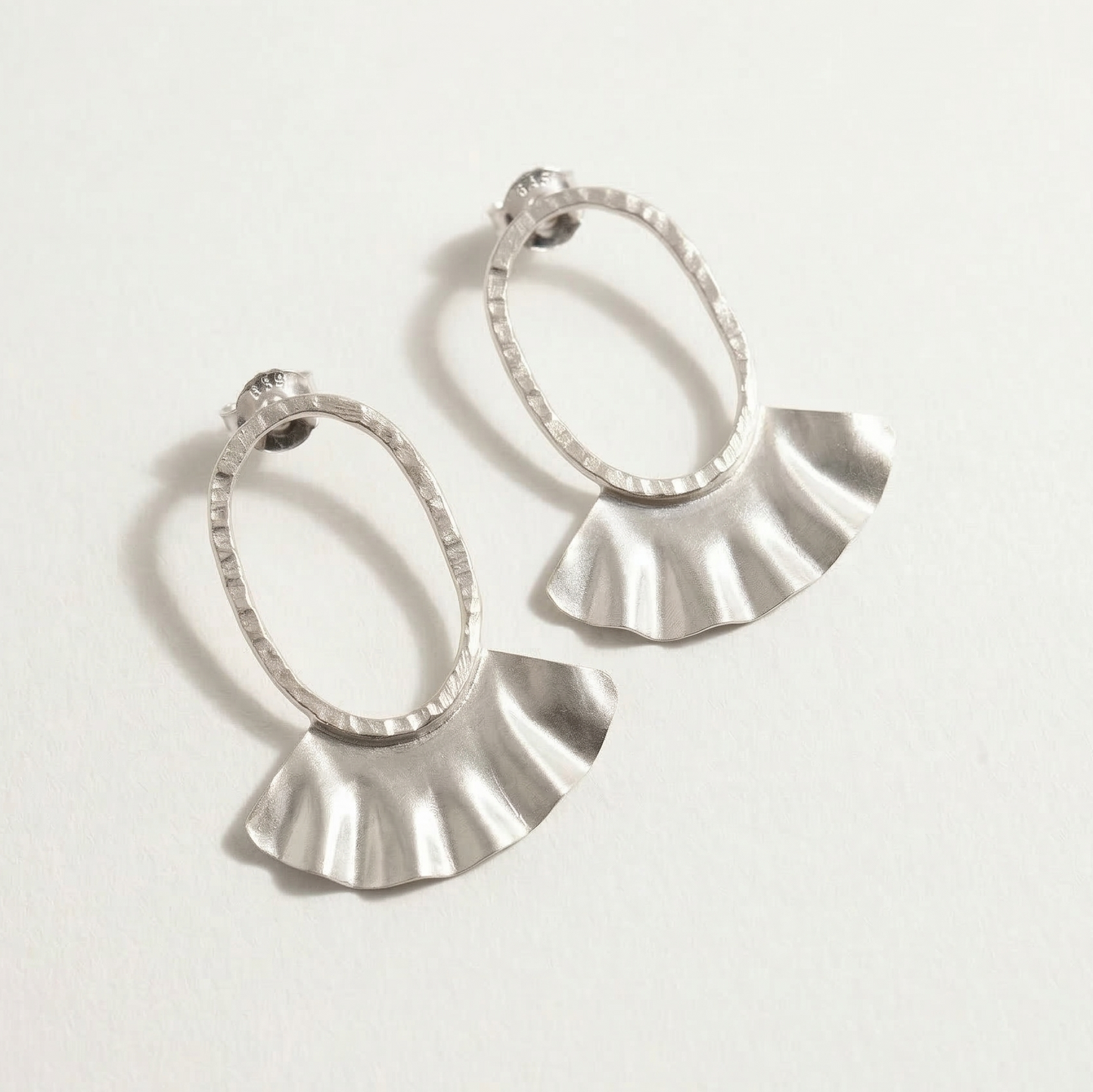 Pair of silver hoop earrings with fan-shaped ends on a light gray background
