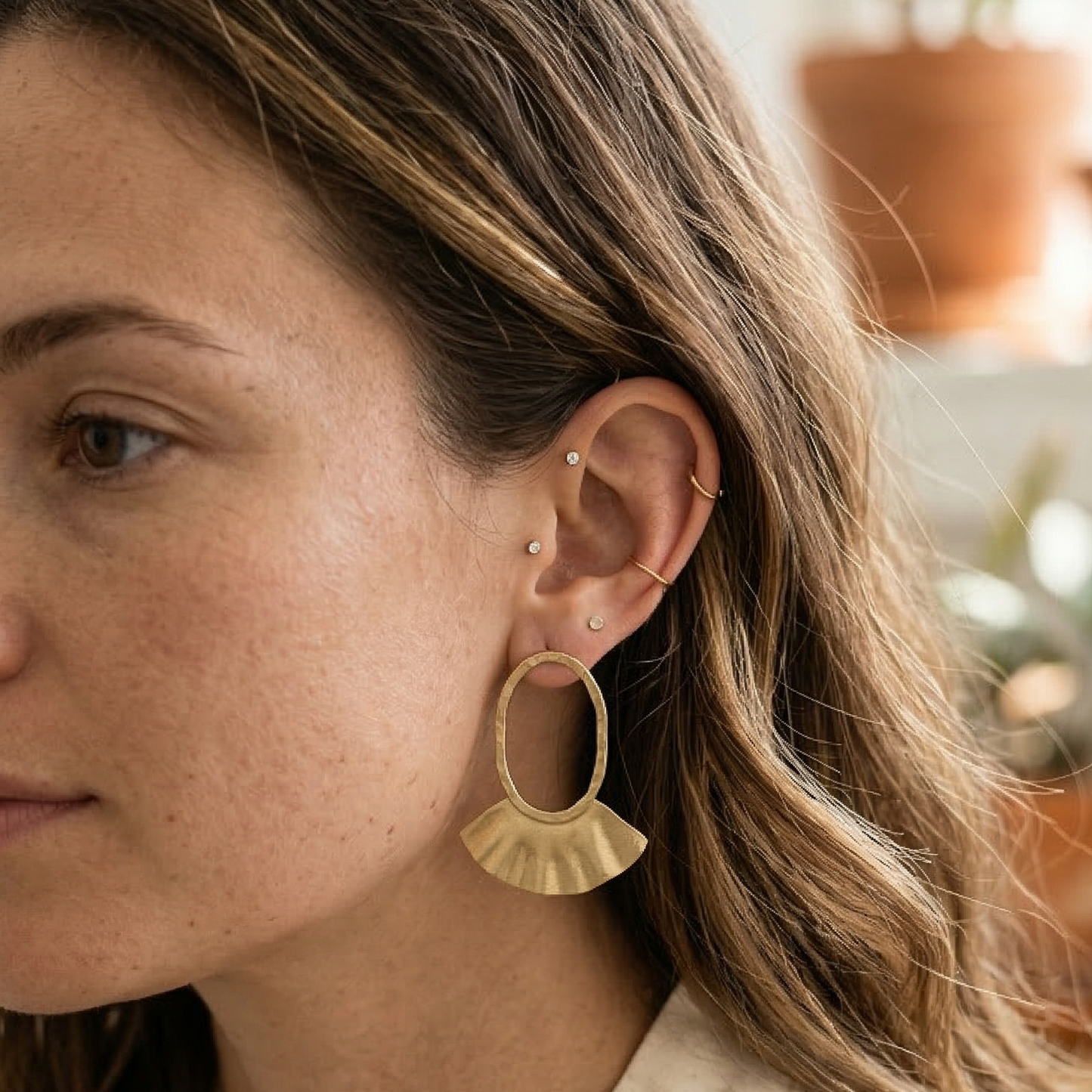 Woman wearing gold hoop earrings with a blurred indoor background