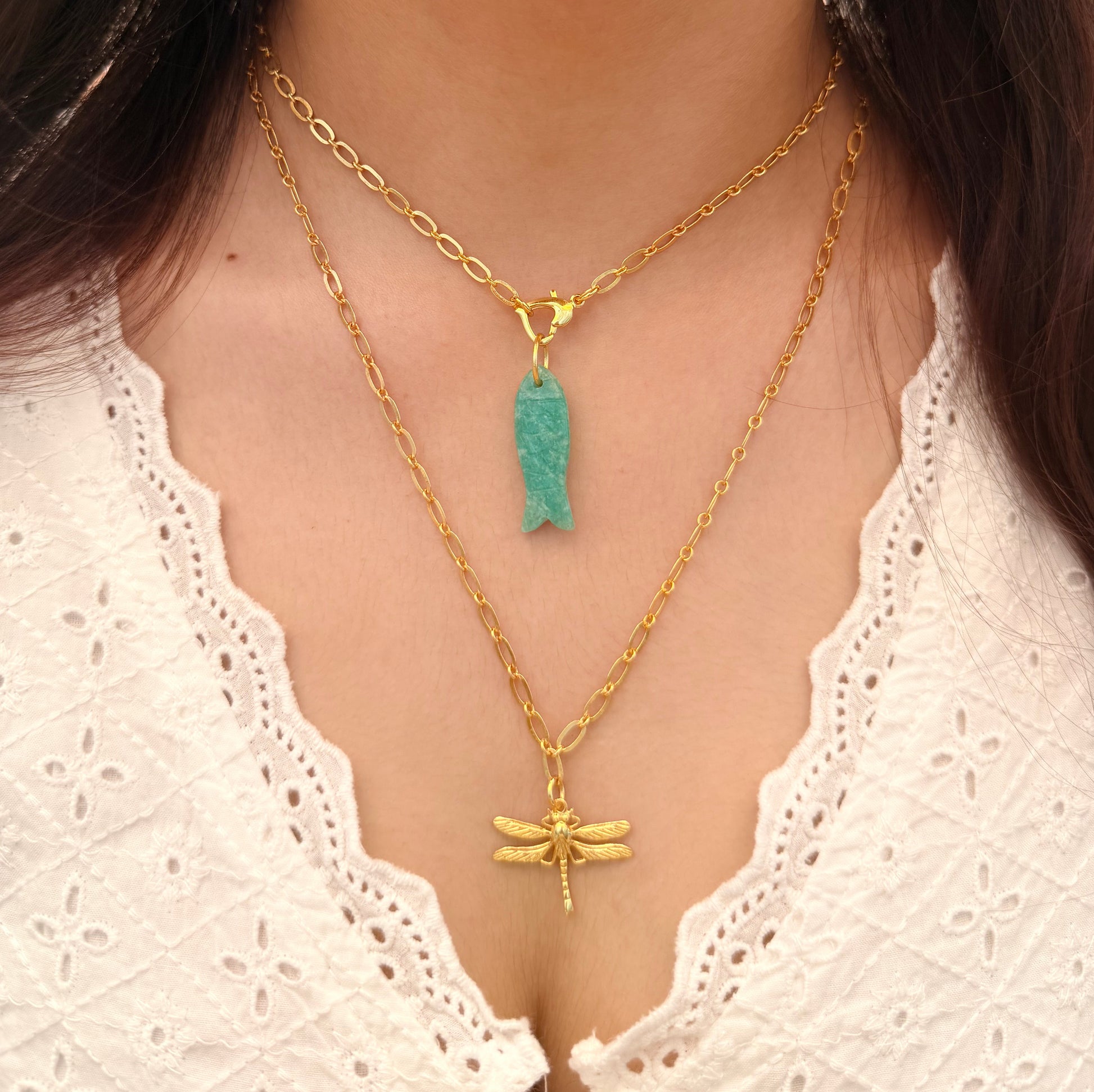 A person wearing two gold necklaces with pendants.