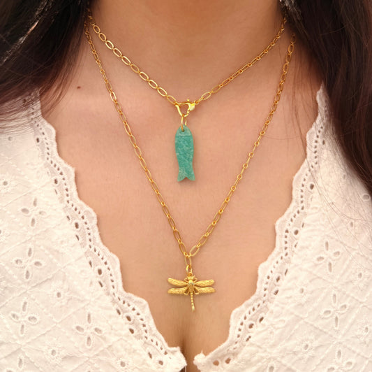 A person wearing two gold necklaces with pendants.