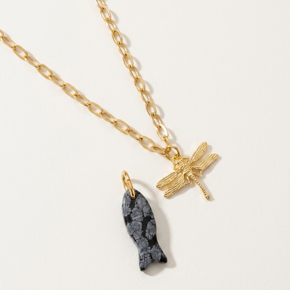 Gold necklace with a fish pendant and a dragonfly pendant on a light gray background