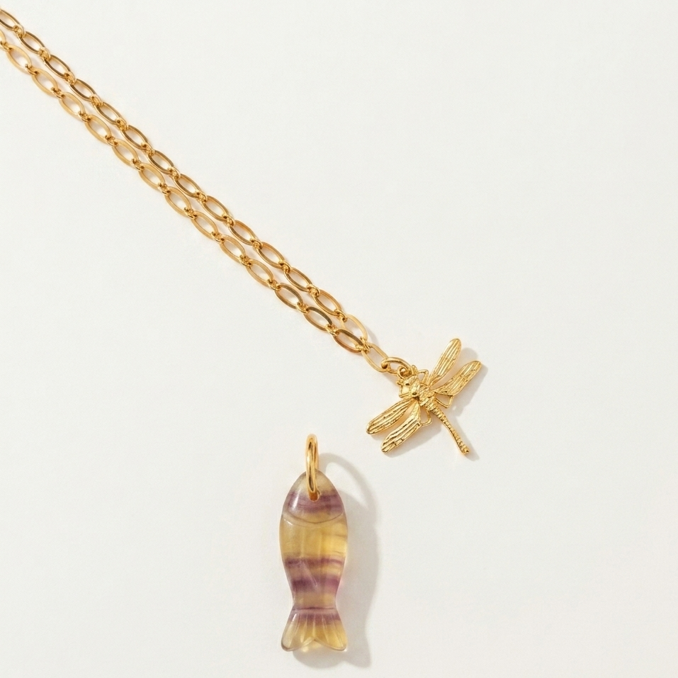 Gold necklace with a fish-shaped pendant and a dragonfly charm on a light gray background