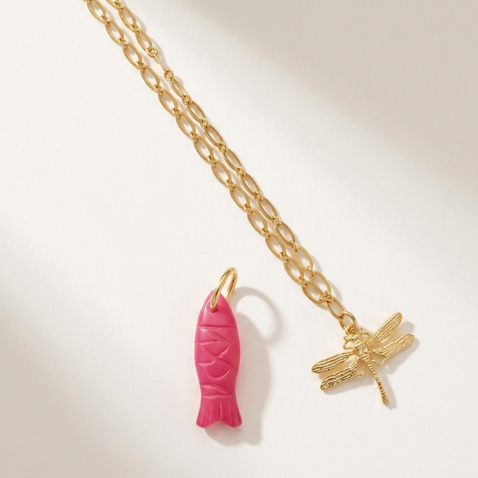Gold chain necklace with pink fish and gold dragonfly pendants on a light background