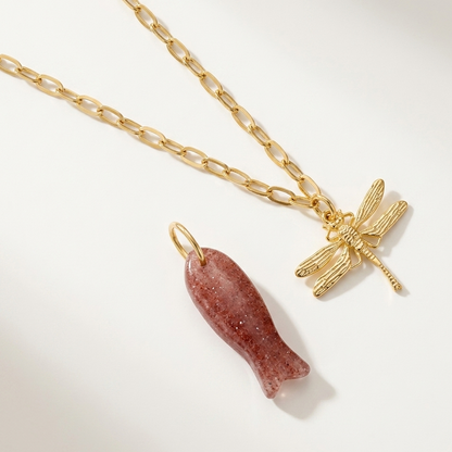 Gold chain necklace with a pink stone pendant and gold dragonfly charm on a white background