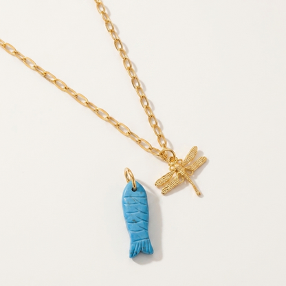 Gold necklace with a turquoise fish pendant and gold dragonfly pendant on a white background