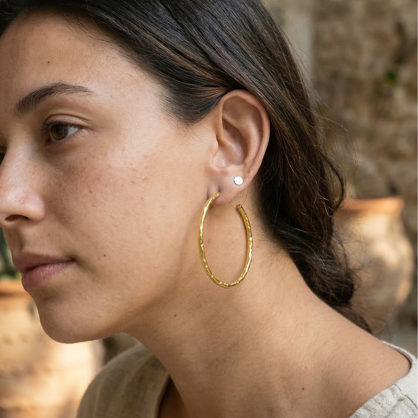 Woman wearing gold hoop earrings with a stone wall and plant in the background