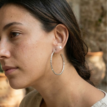 Woman wearing hoop earrings with a stone wall and plant in the background