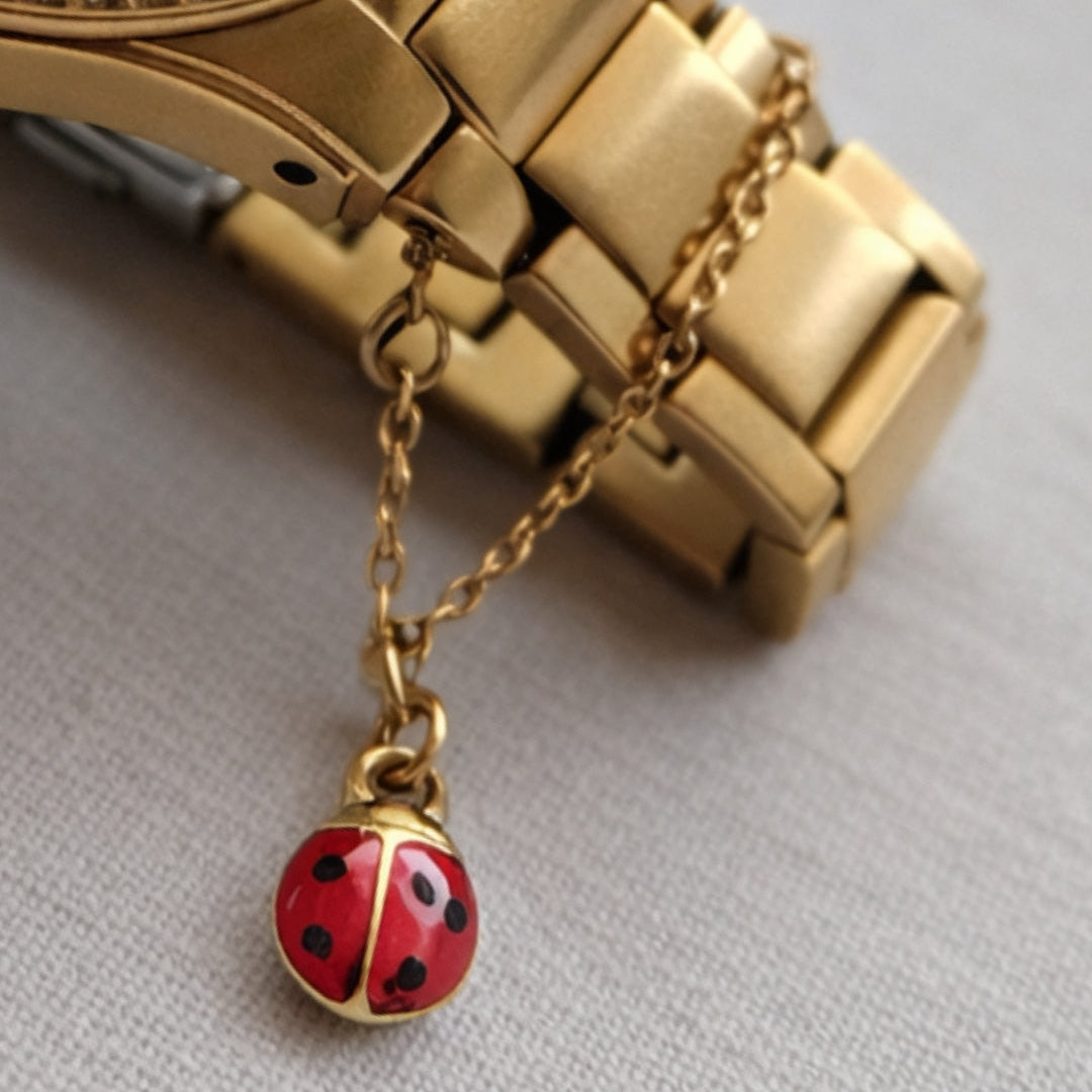 Gold watch with a red ladybug charm on a light gray background