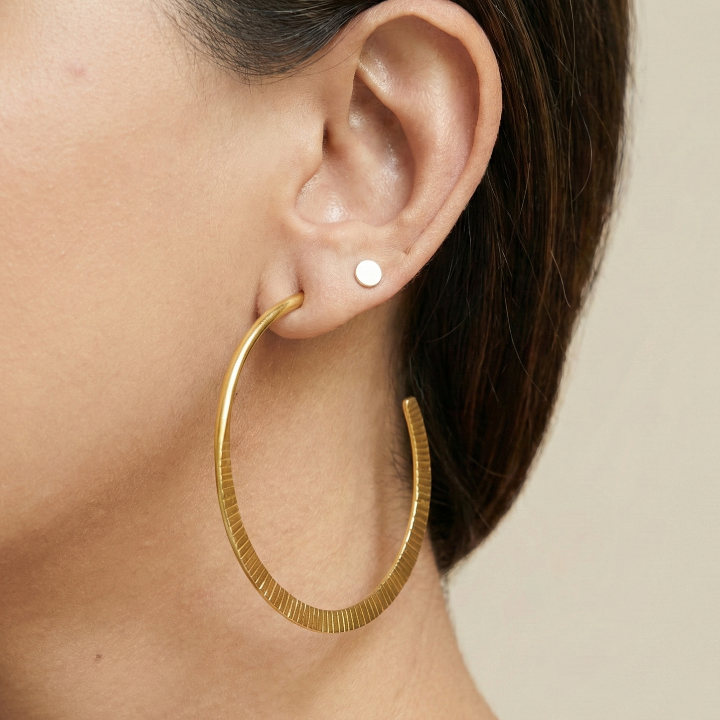 Gold hoop earring worn by a person on a neutral background
