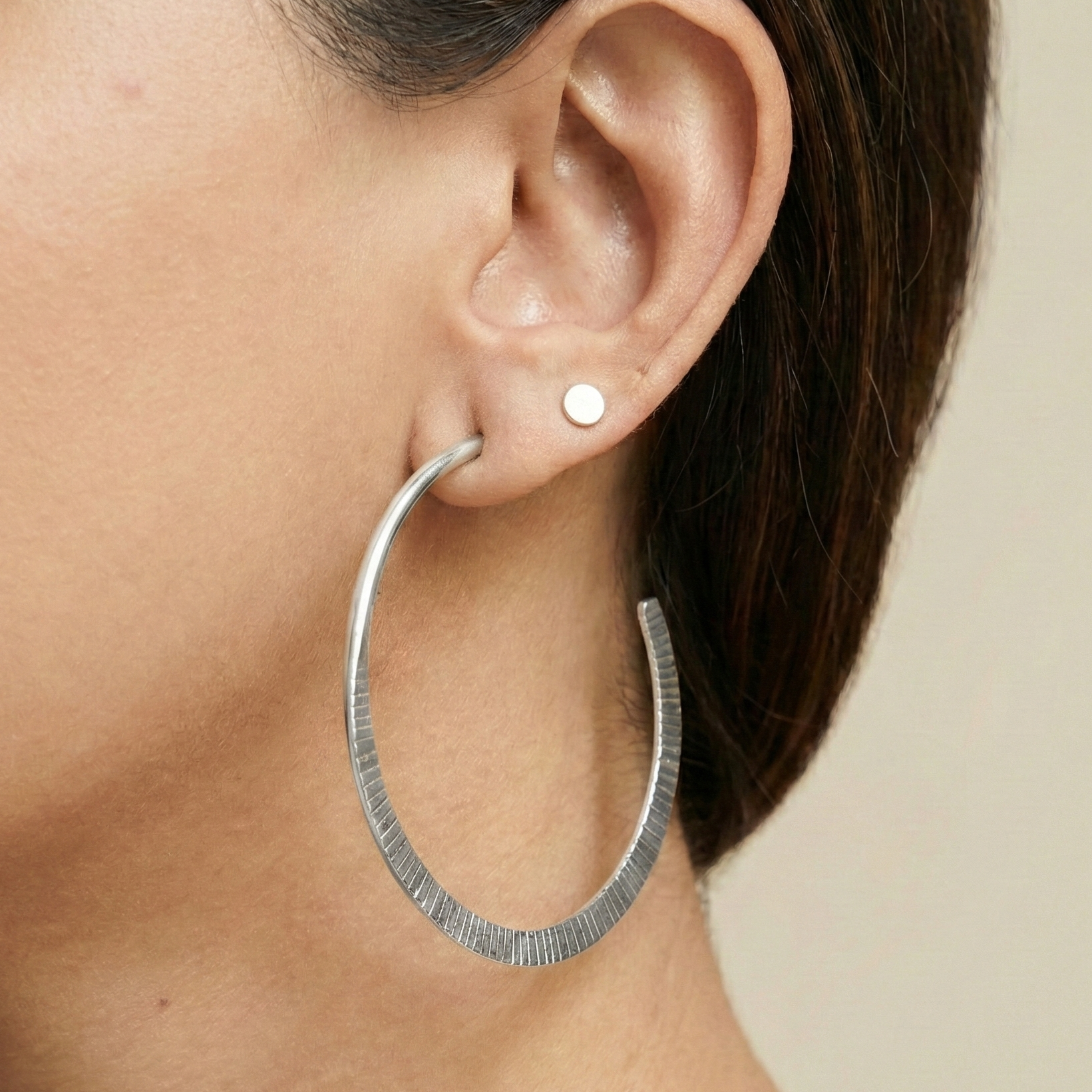 Silver hoop earring worn by a person on a neutral background