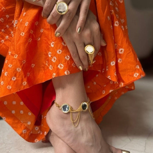 Close-up of a person's feet wearing gold anklets and rings, with an orange garment.