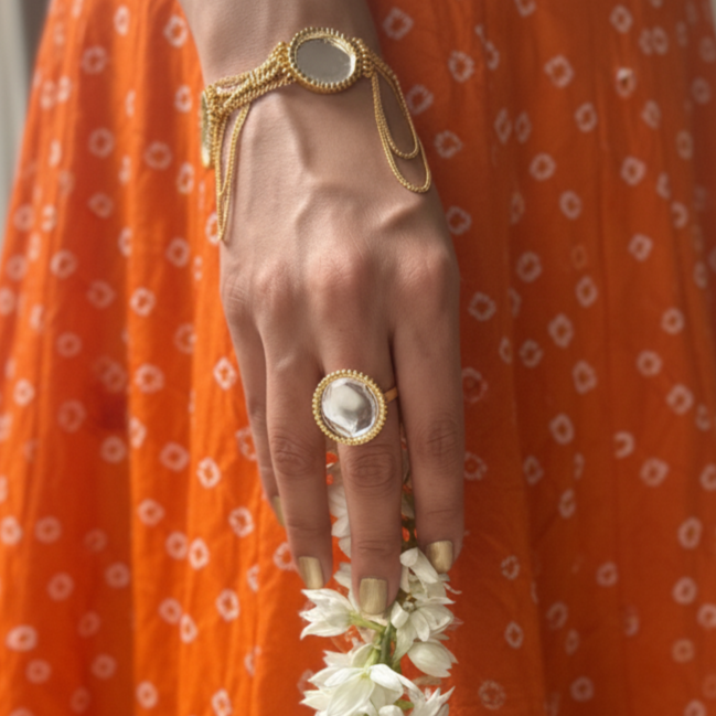 Person wearing an orange traditional outfit with a gold bracelet and ring, holding a white flower garland.