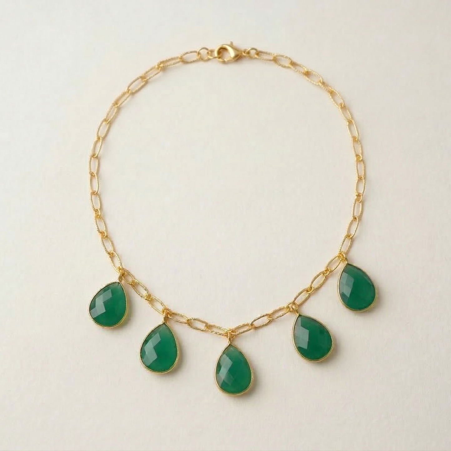 Gold necklace with green teardrop-shaped gemstones on a light beige background