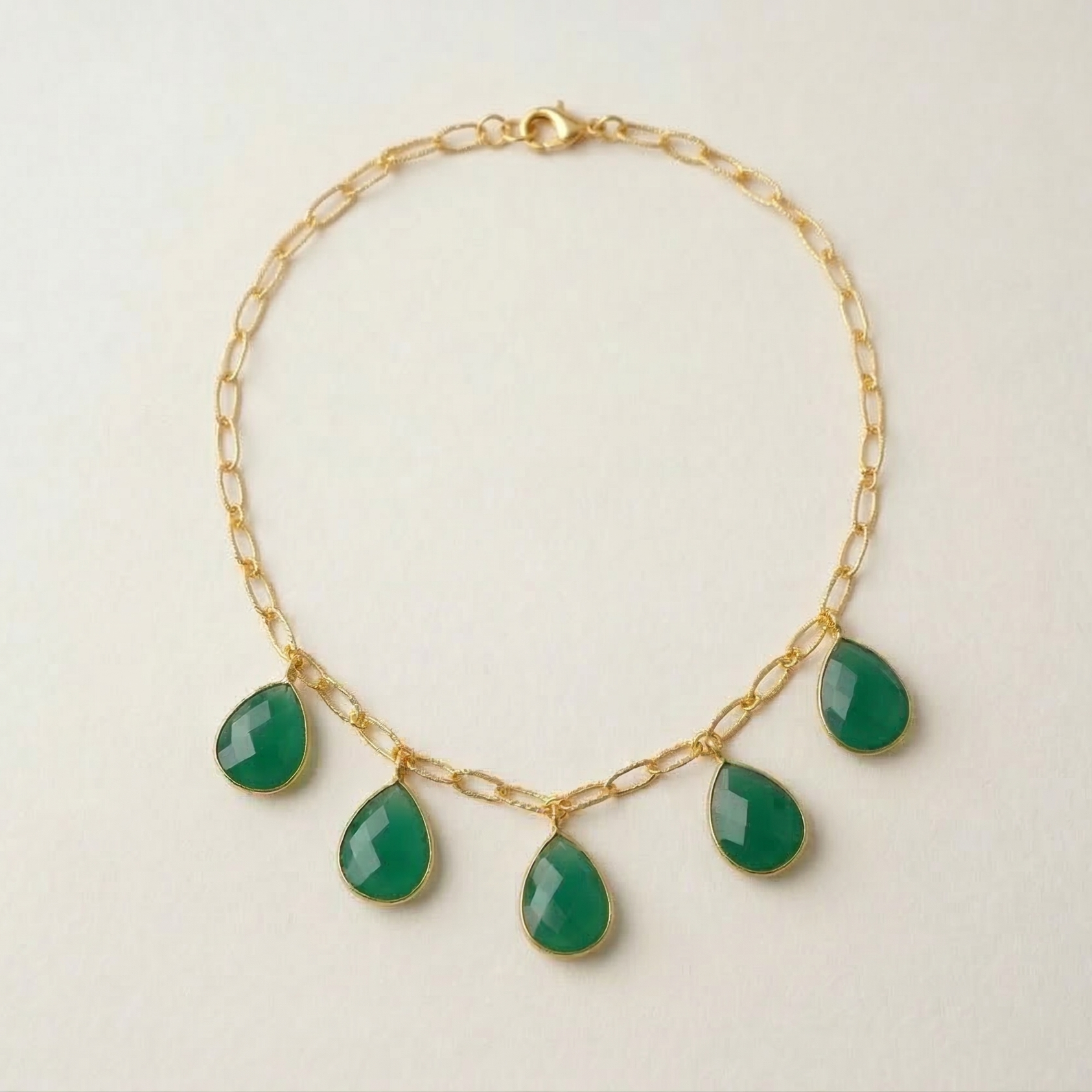 Gold necklace with green teardrop-shaped gemstones on a light beige background