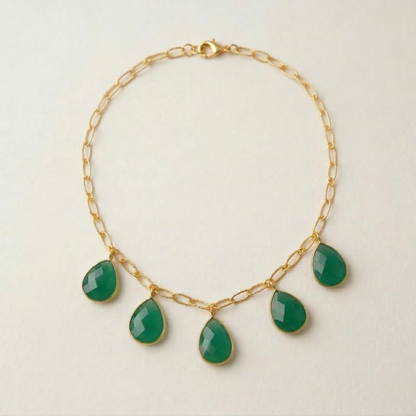 Gold necklace with green teardrop-shaped gemstones on a light beige background