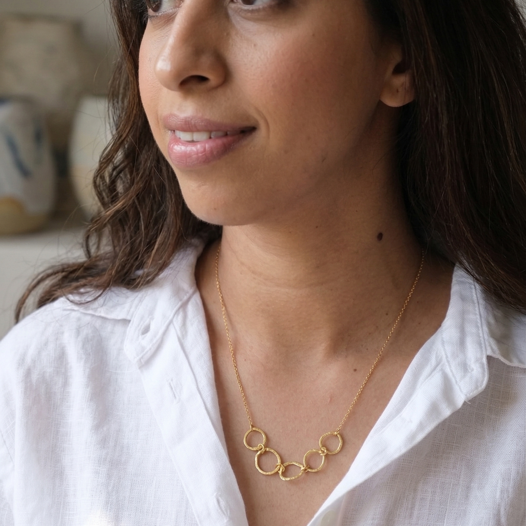 Woman wearing a gold necklace with a white shirt indoors